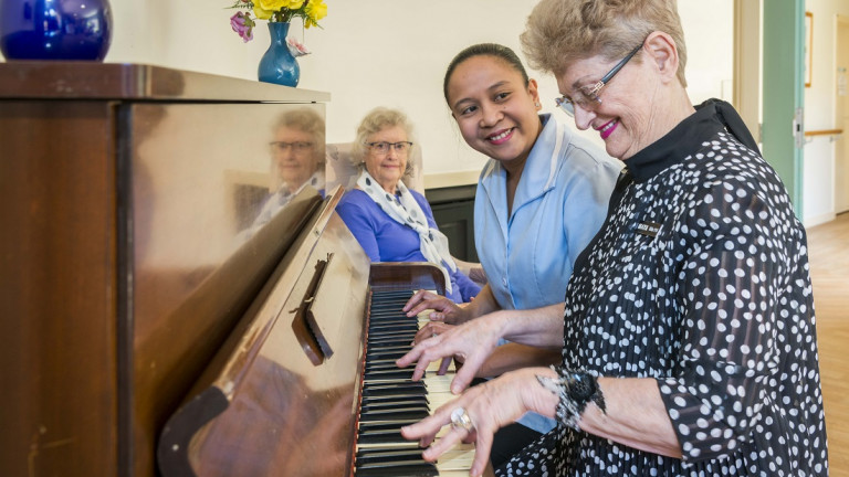 Woman playing piano with support worker next to her