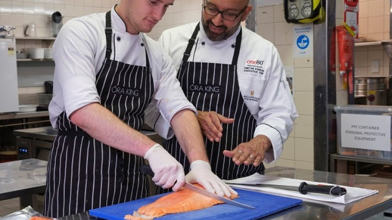 Kitchen worker filleting a salmon with chef looking on