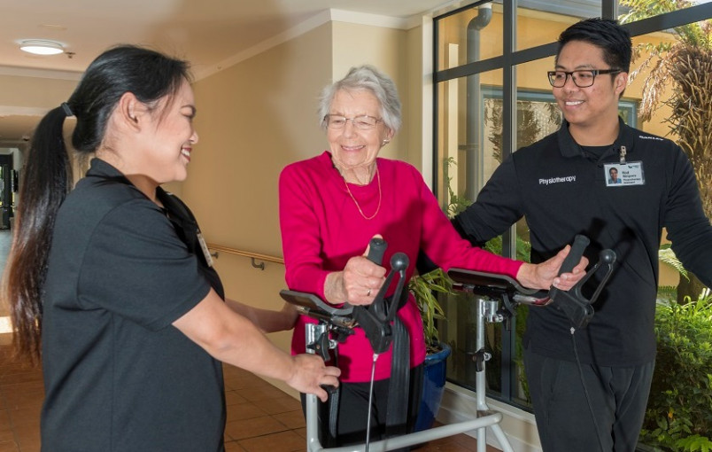 A lady with a walker flanked by two migrant aged care workers