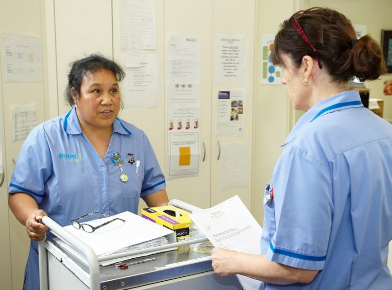 Supervisor giving instructions to a migrant aged care worker standing behind a trolley