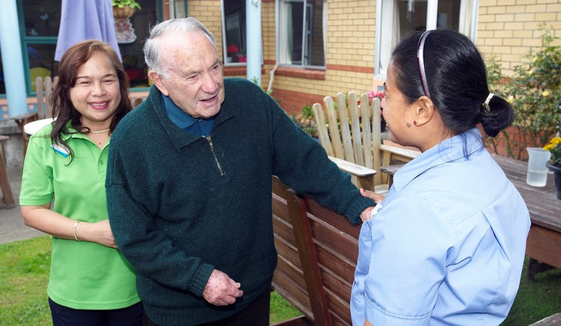 2 care workers talking with elderly man in the rest home garden.