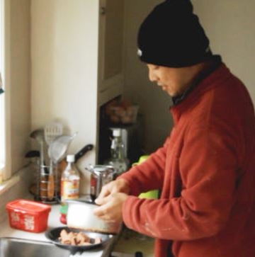 Filipino worker in his kitchen wearing a wooly hat and fluffy jacket