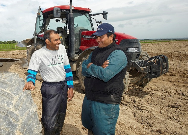 Dairy workers talking beside a tractor