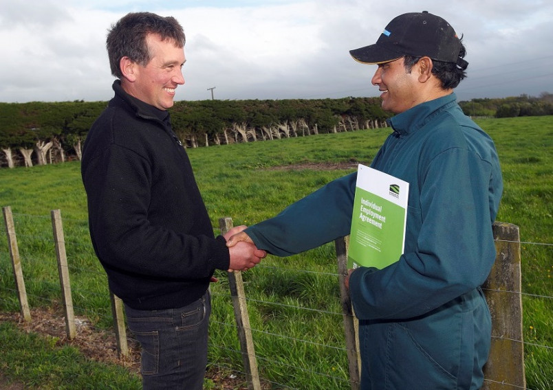 Farmer and migrant worker shaking hands - worker holding an employment agreement