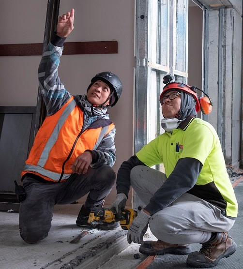 2 migrant workers on a building site - one pointing something out to the other worker