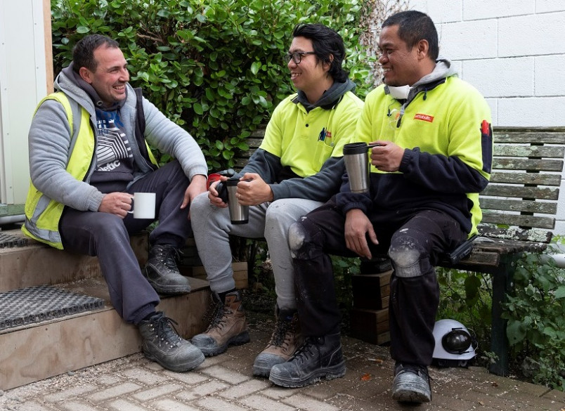 3 migrant workers sitting outside during a break and laughing