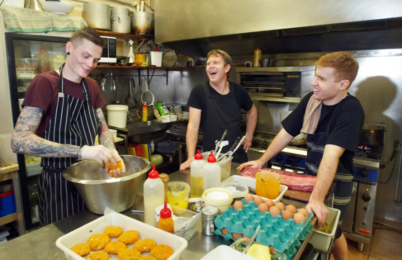 3 cafe workers laughing in the kitchen while doing prep