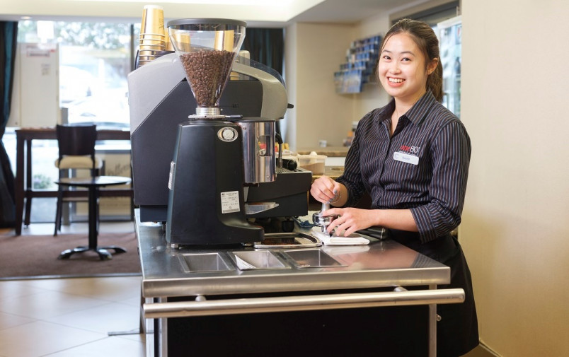 Migrant cafe worker smiling at camera from behind the coffee grinder in hotel foyer