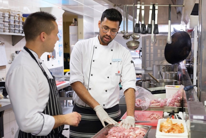 Migrant worker showing another worker how to prepare chicken pieces safely