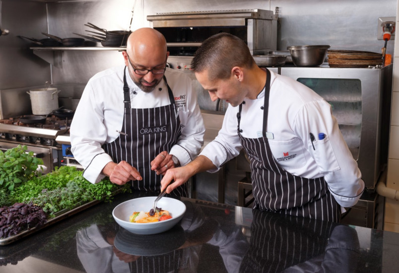 Senior chef showing young chef how to plate up a salad