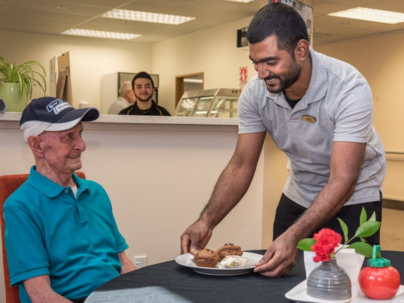 An indian aged care worker serving a village resident a meal in the dining room.