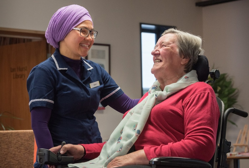 Migrant aged care worker smiling and talking to elderly woman in wheelchair
