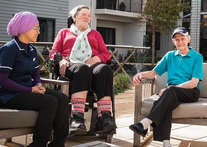 A migrant aged care worker having a break in the sun and chatting to 2 elderly residents.