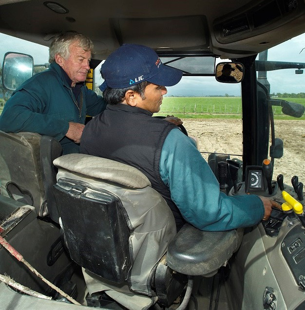 Farmer showing a migrant worker how to use a new tractor