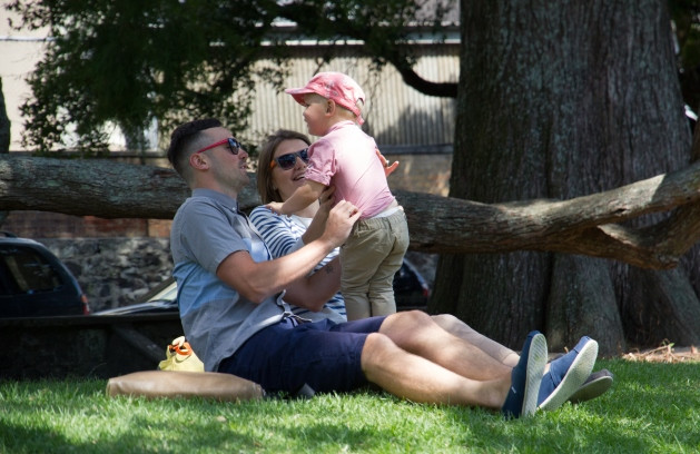 A man holding a child and a woman sitting under a tree