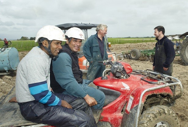 Migrant workers on a farm quad bike with employers behind them