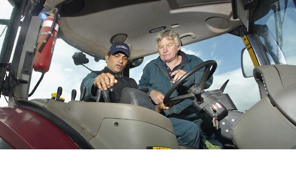 An employer shows a migrant employee the controls of a tractor