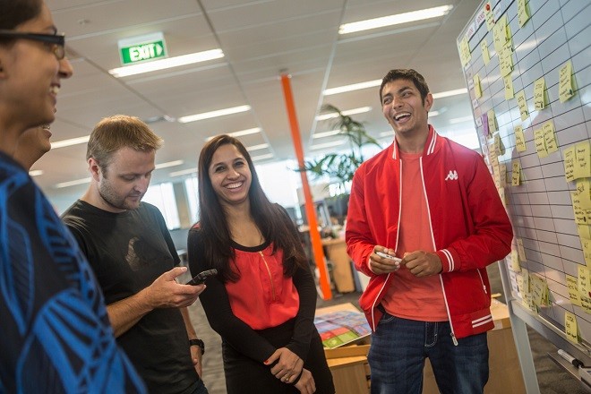 Five office workers meet around a kanban board